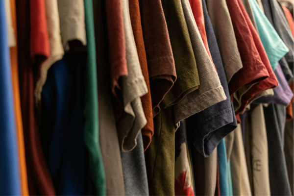 A close-up view of various colorful t-shirts hanging neatly in a closet, showing diverse fabric textures and shades.