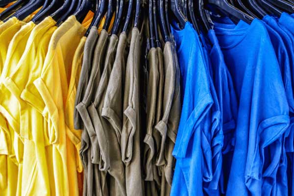 Yellow, dark green, and blue t-shirts hanging from clothes hangers